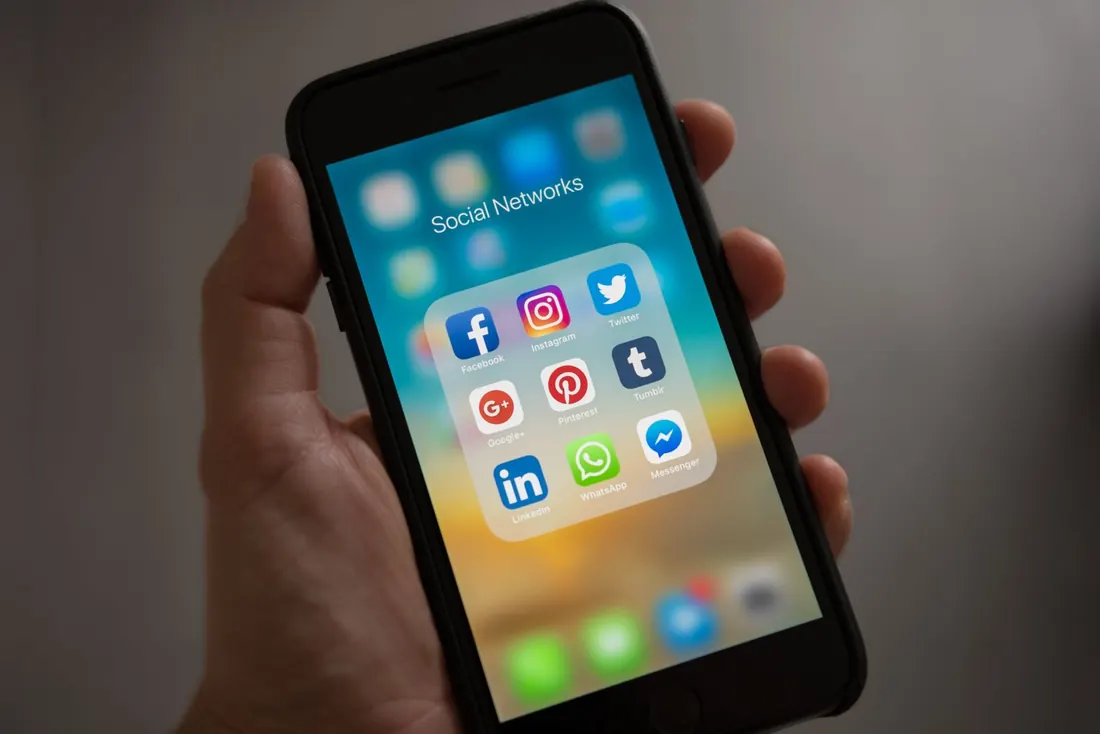 Mão segurando um celular com aplicativos de redes sociais
