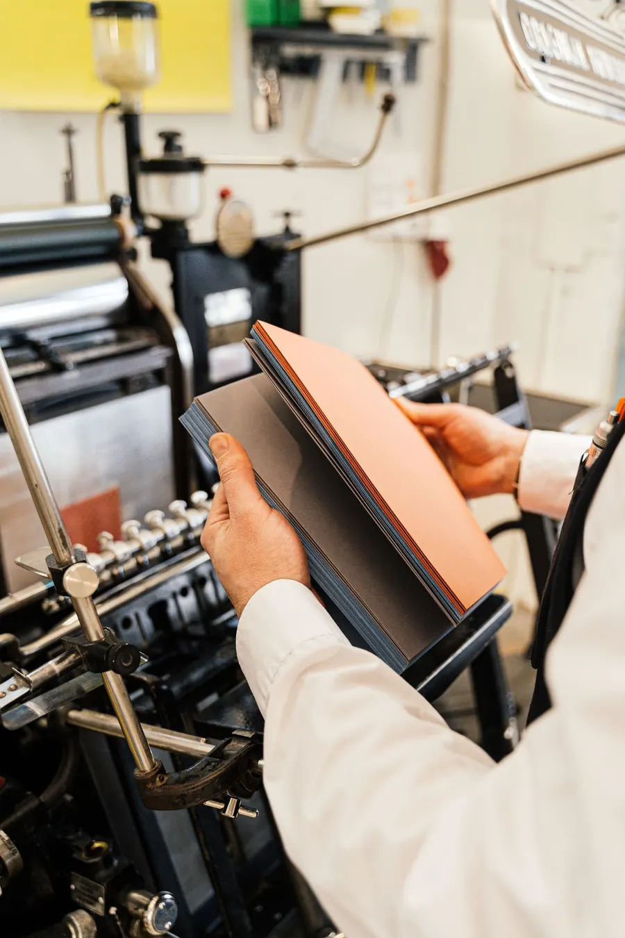 Profissional segurando folhas recém-impressas ao lado da máquina